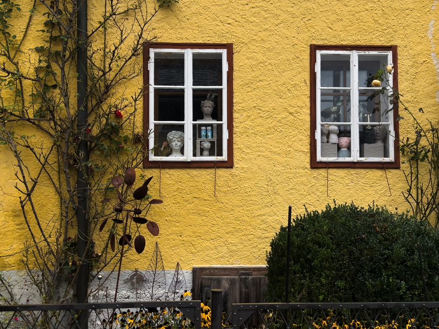 A vibrant yellow house facade with two white-framed windows displaying decorative busts.