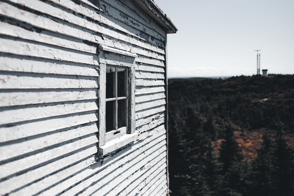 A weathered wooden house with peeling paint overlooks a vast countryside and a distant tower.