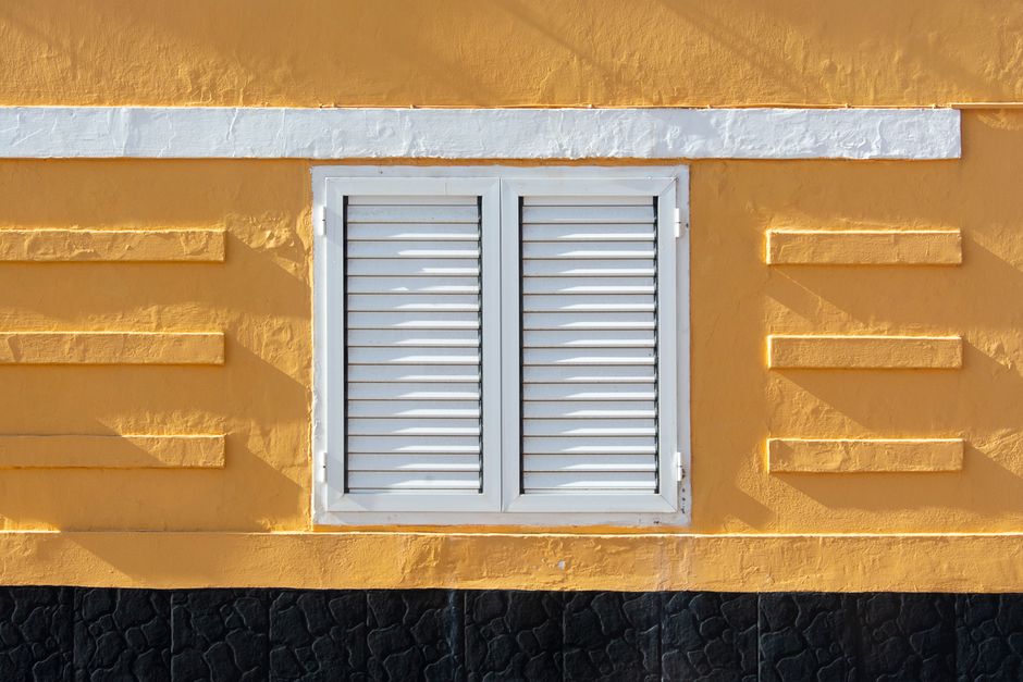 Close-up of a yellow wall with white shutters, minimalistic design and strong geometric patterns.