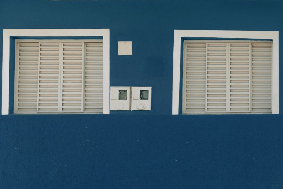 A simple blue wall featuring two white shuttered windows, offering a minimalist aesthetic.